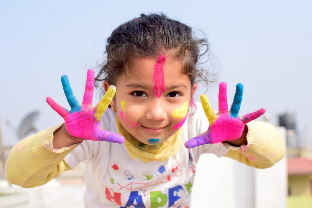 young girl with paint on her fingers and face in a t shirt with the word happy on the front of it